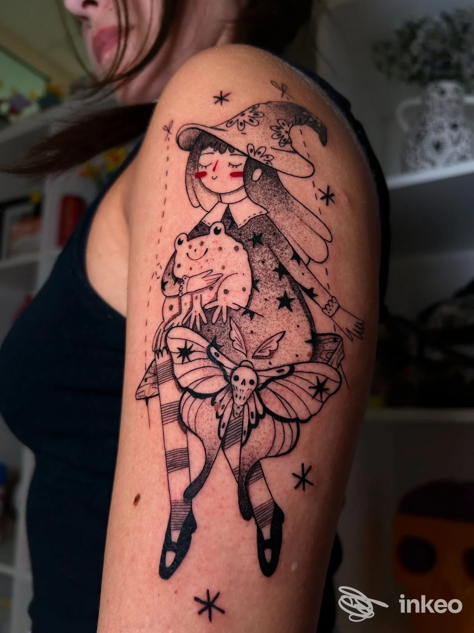 Tattoo su braccio sinistro di una persona, disegno illustrativo con figura femminile, cappello a punta, farfalle e stelle, linee nette in stile cartone; colore principale: nero.