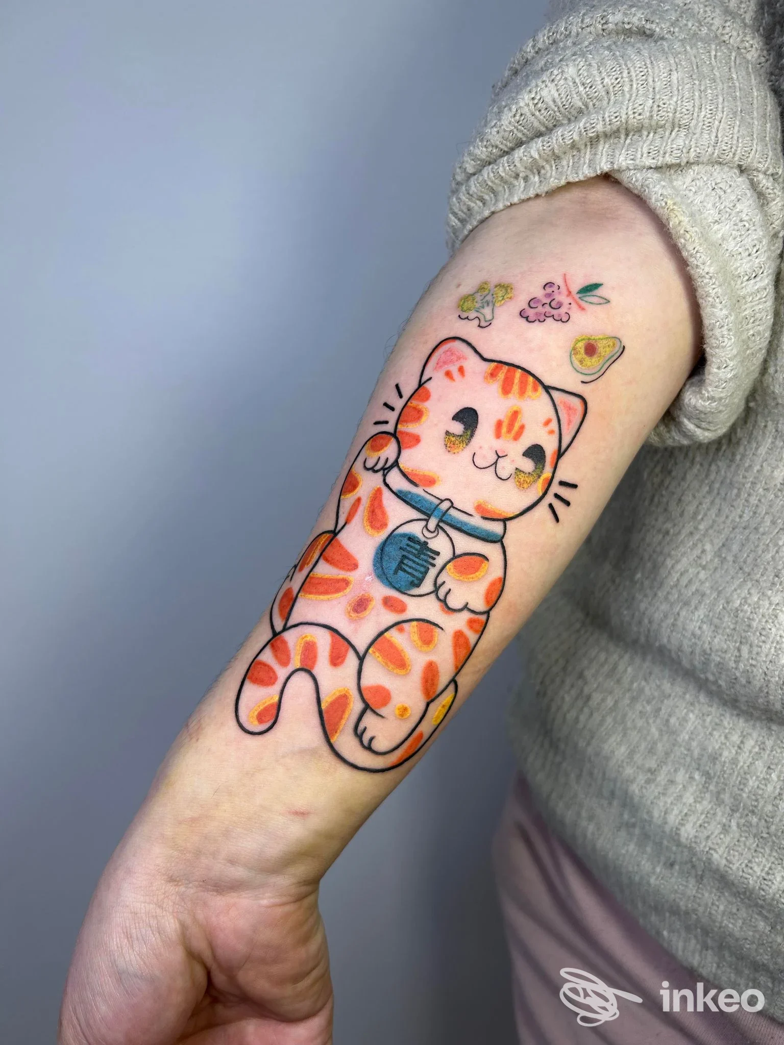 Tattoo colorato di gatto stilizzato sul braccio, disegno vivace su pelle, con dettagli vivaci e colori orange, nero e azzurro.