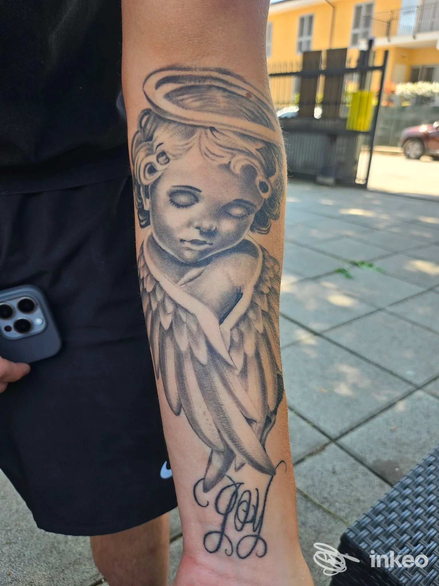 Angelo tatuato sull'avambraccio di una persona, tatuaggio in bianco e nero con dettagli delle ali e del volto infantile, stile classico, visibile in strada, studio Dave Tattoo Studio a Giulianova.