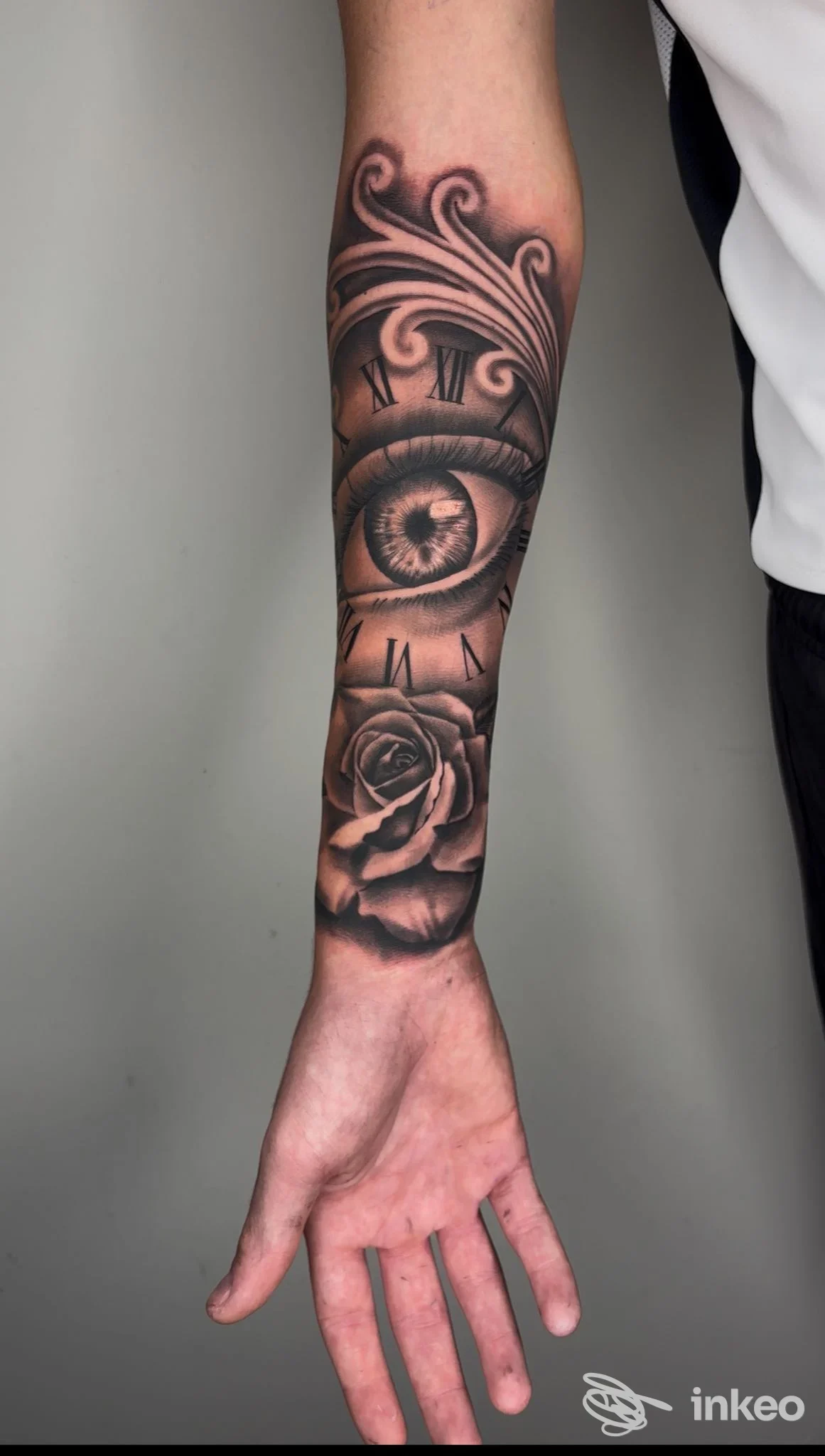Tattoo visibile sul braccio: occhio centrale circolare, rose e motivi ornamentali in tonalità scure, pelle ben curata e dettaglio realistico.