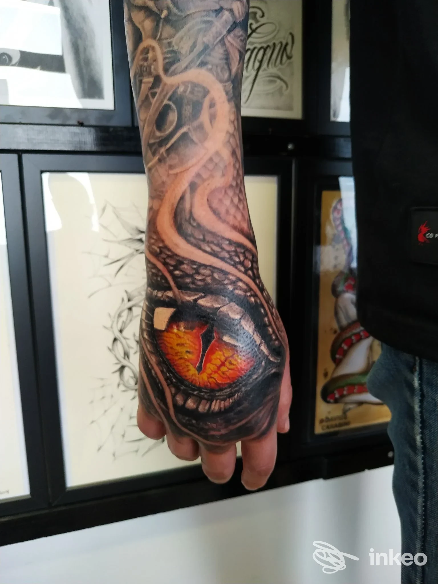 Avamposto su palmo visibile un tatuaggio realistico di un serpente con squama e un occhio arancione intenso sul dorso della mano, realizzato in tonalità scure e dettagli anatomici.