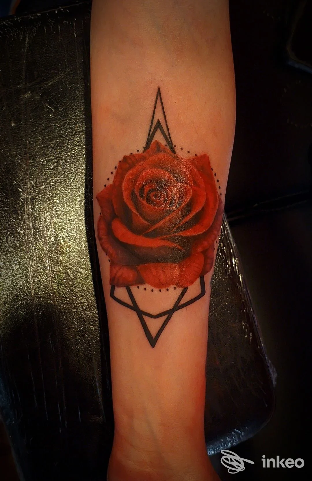 Tatuaggio su avambraccio: rosa rossa con geometrie geometriche nere, realizzato sulla pelle; si osserva lo sfondo della poltrona del studio Metropolis Tattoo Studio a San Benedetto dei Marsi.