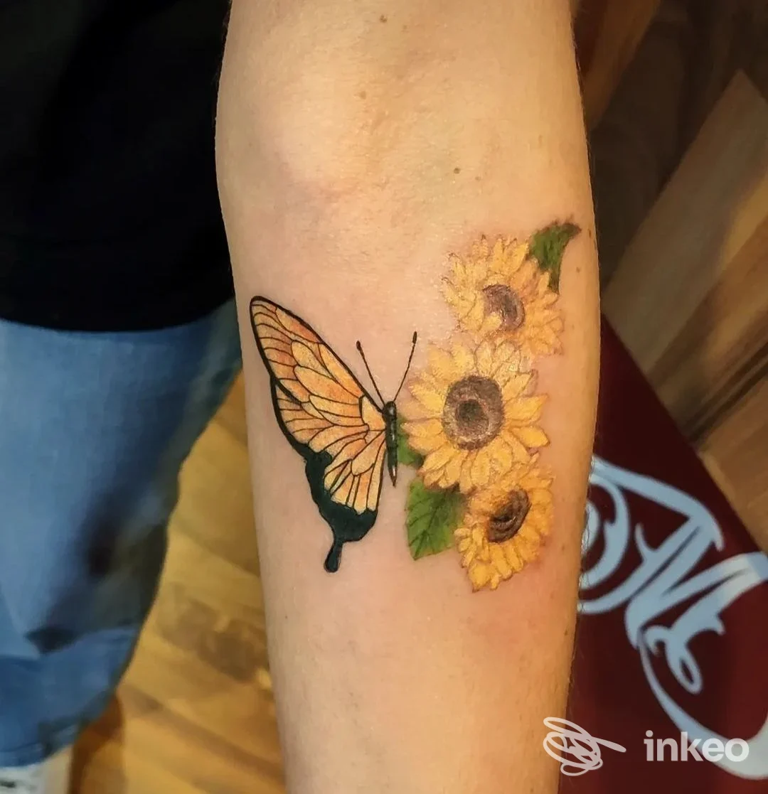 Inchiostro visibile su braccio: un delicato tattoo raffigurante una farfalla accanto a un grappolo di girasole, eseguito sulla pelle.