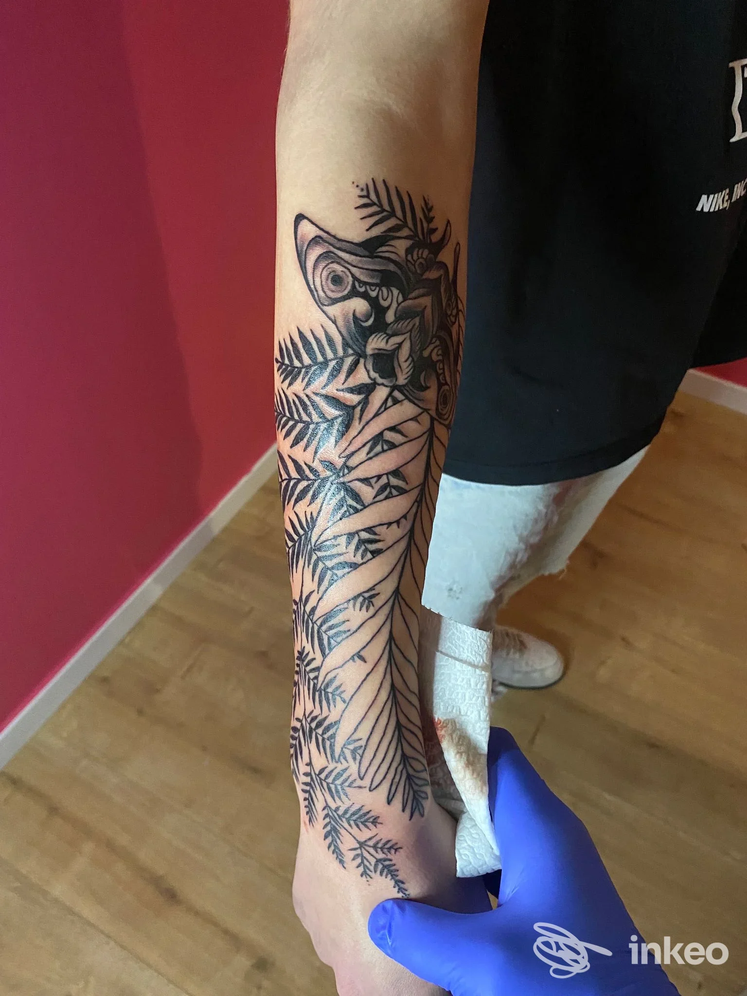 Tatuaggio realistico di stile botanico sulla gamba sinistra, fiori e foglie in nero, eseguito in uno studio di tatuaggi; visibile la pelle e il disegno definitivo. Studio Arkham 14, Pescara.