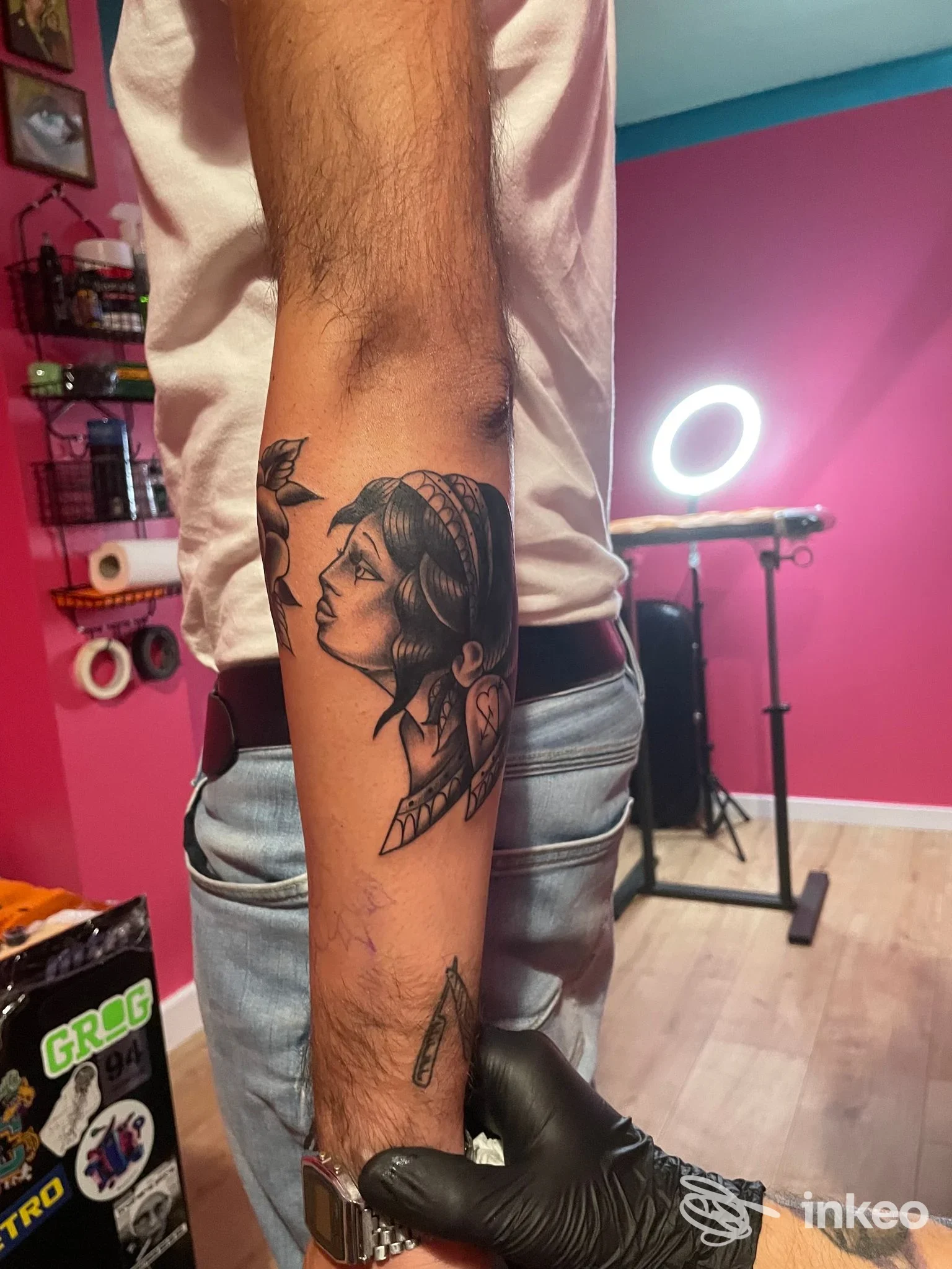 Avambraccio di un uomo con un tatuaggio ritratto realistico in bianco e nero di una figura femminile, bordi netti e sfumature luminose nell'ambiente di uno studio.
