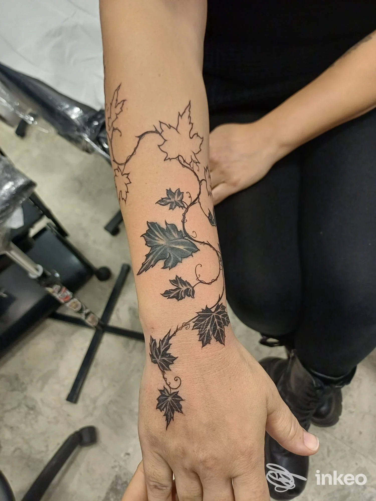 Braccio di una persona con un tatuaggio a foglie di acero che si sviluppa lungo avambraccio, inchiostro nero su pelle chiara, scatto in studio.
