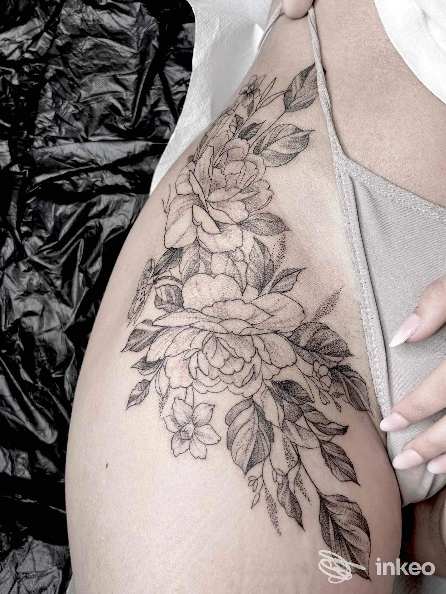 Tattoo floreale a colori neri su pelle chiara lungo la spalla e la gamba di una persona, con dettagli di fiori e foglie.