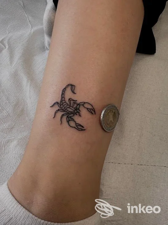 Tattoo di uno scorpione su pelle, posizionato vicino alla caviglia, visibile su una gamba con una moneta accanto per confronto delle dimensioni; studio One Love Ink, Montesilvano.