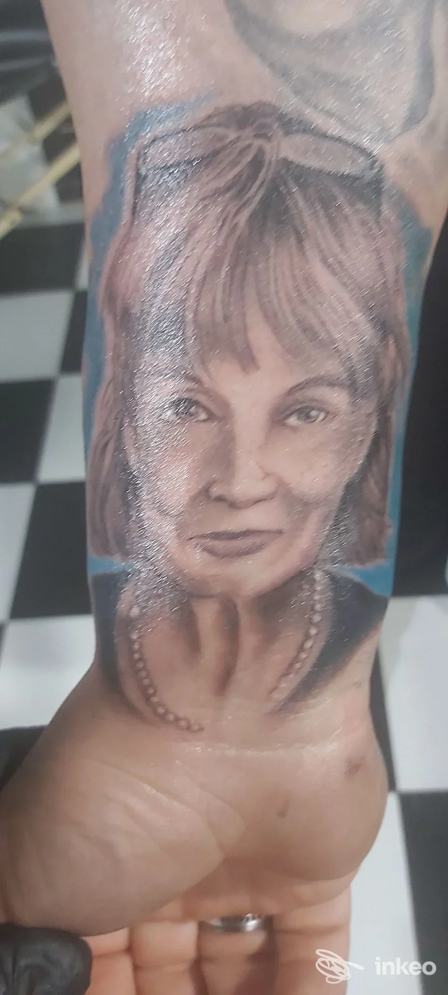 Ritratto realistico di donna tatuato sull’avambraccio, con sfondo blu, visibile su pelle concreta; studio Old Tip Tattoo, Ortona.