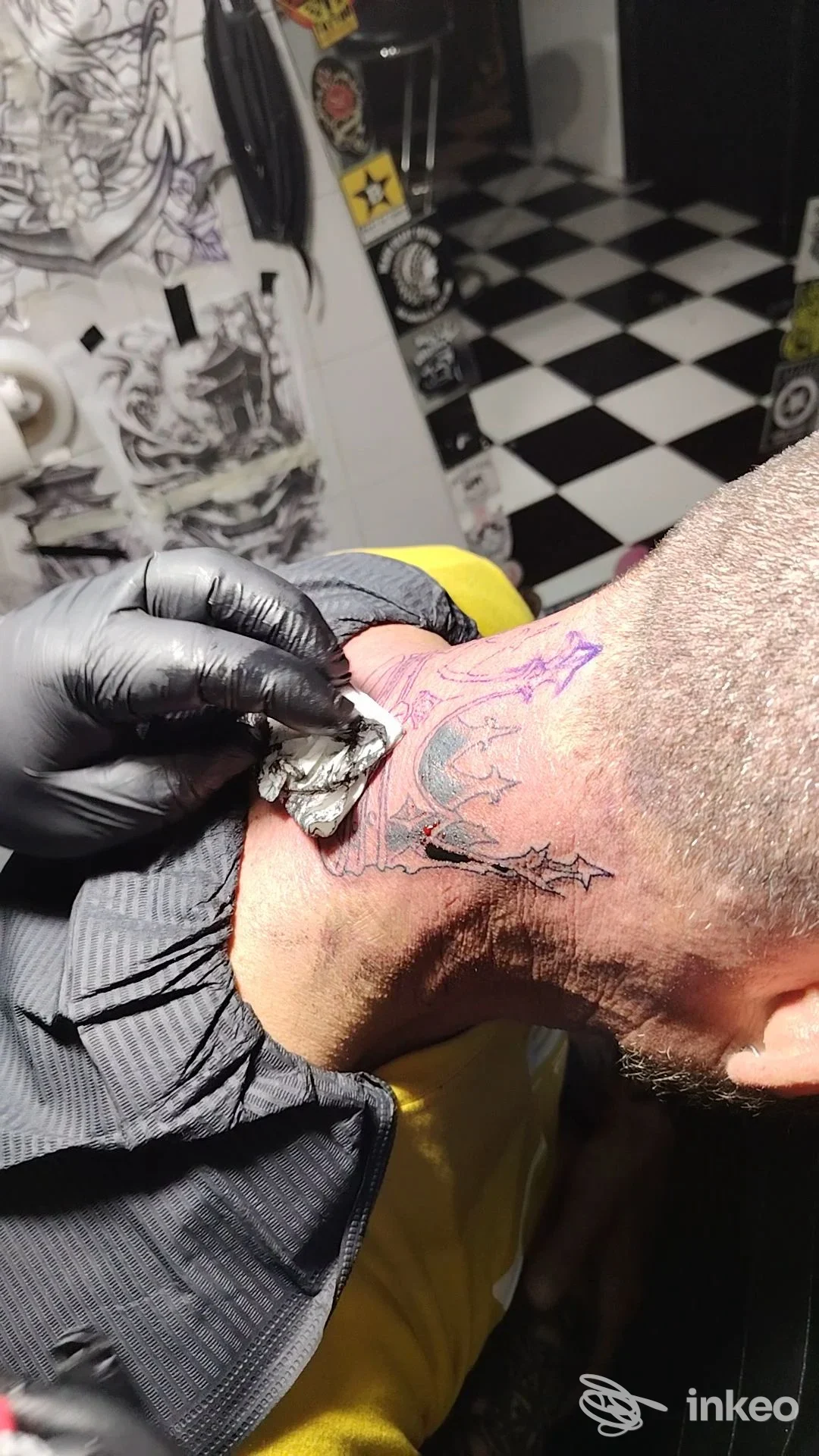 Tatuaggio in corso sul collo, linea di contorno viola su pelle, guanti neri dell’artista: studio Old Tip Tattoo, Ortona.