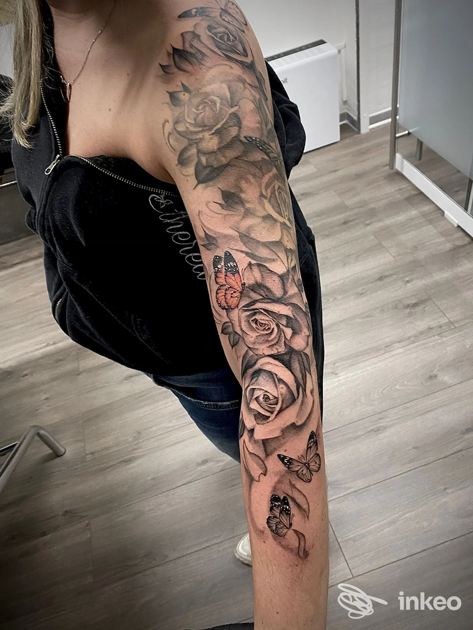 Brascio sinistro visibile con un grande tatuaggio a tema rose elaborate e farfalle, braccio interamente coperto da tattoo, scatto in studio, colori neri e grigi ben definiti.