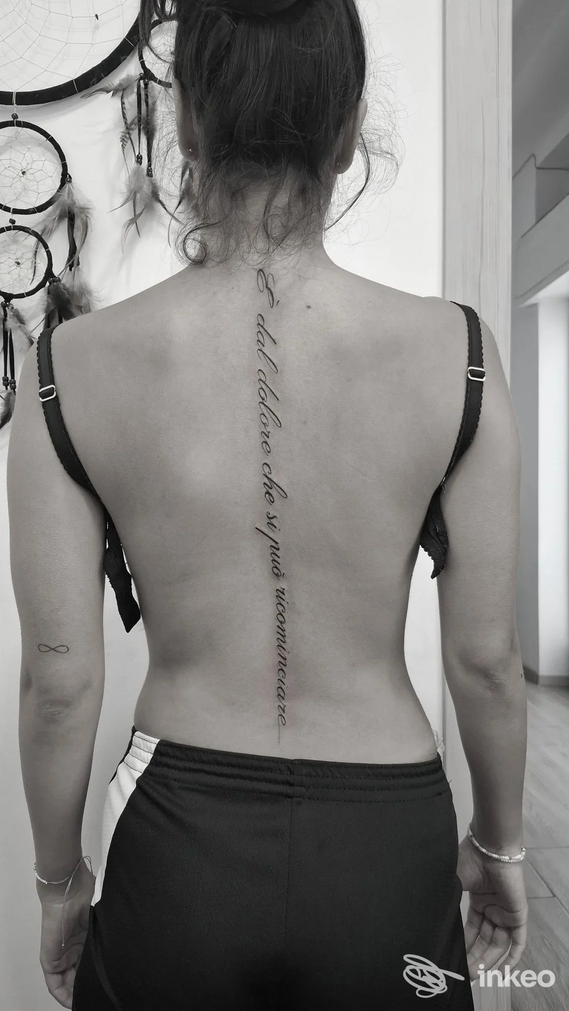 Una persona vista di schiena mostra un tatuaggio verticale lungo la colonna vertebrale, senza viso visibile.