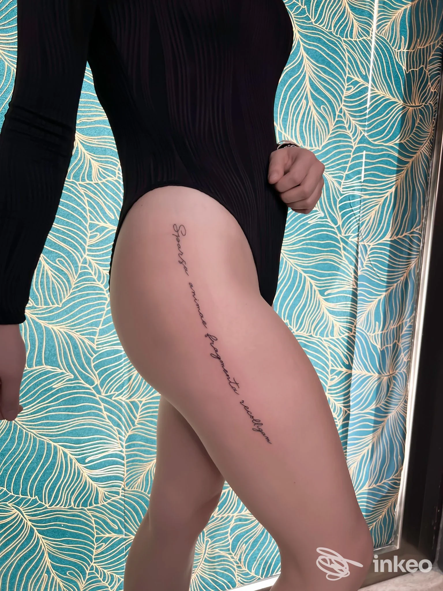 Tattoo tradizionale lungo la coscia di una persona in body tight, firma stilizzata in corsivo lungo la gamba, sfondo con carta da paravento azzurra. Studio Insider Tattoo, Crotone.