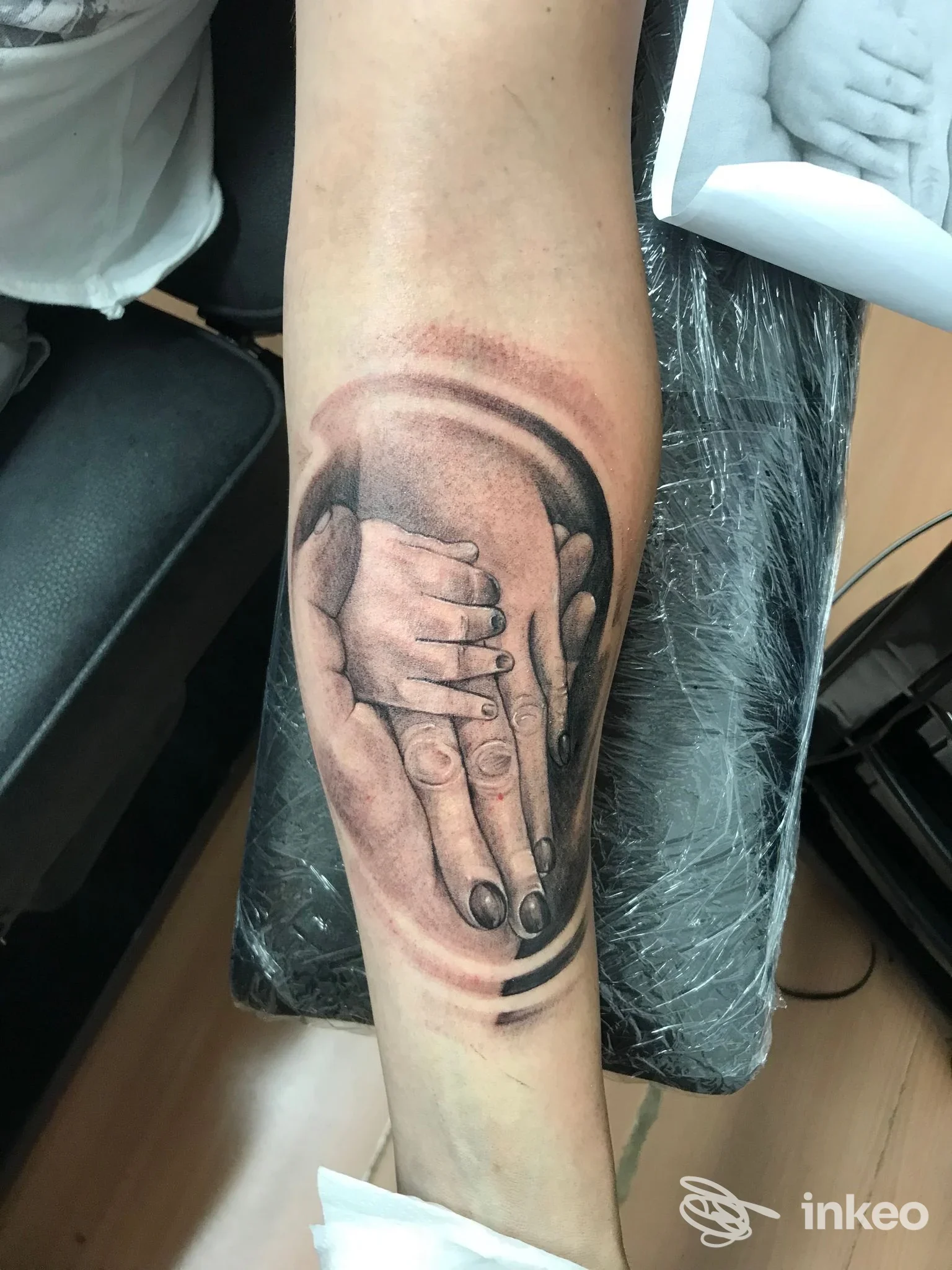 Tatuaggio raffigurante due mani che si prendono, realizzato sulla pelle dell'avambraccio, tonalità grigio-nere, con sfumature e dettaglio delle dita.