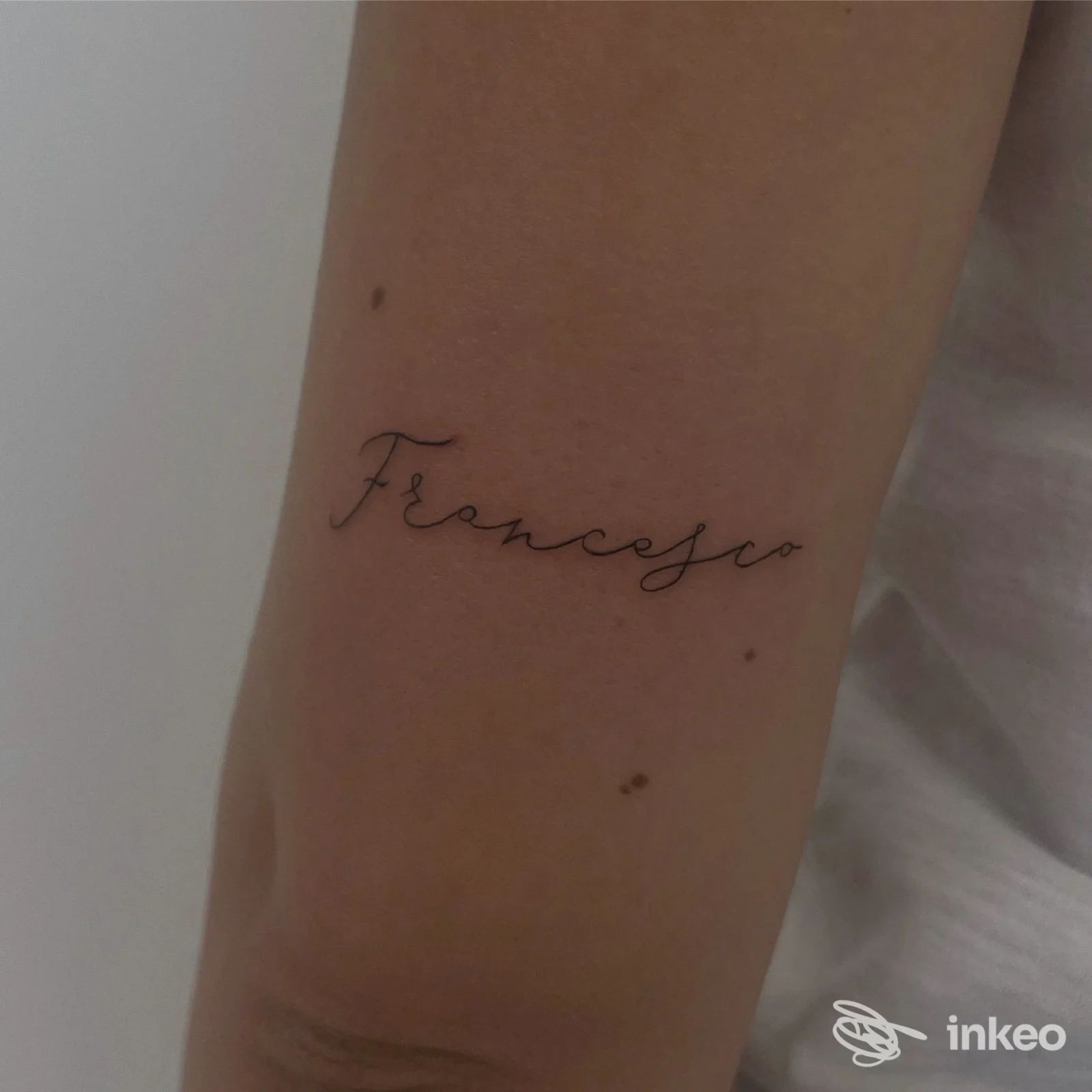 Tattoo in corsivo nero sull'avambraccio, pelle liscia visibile, linea sottile e dinamica.