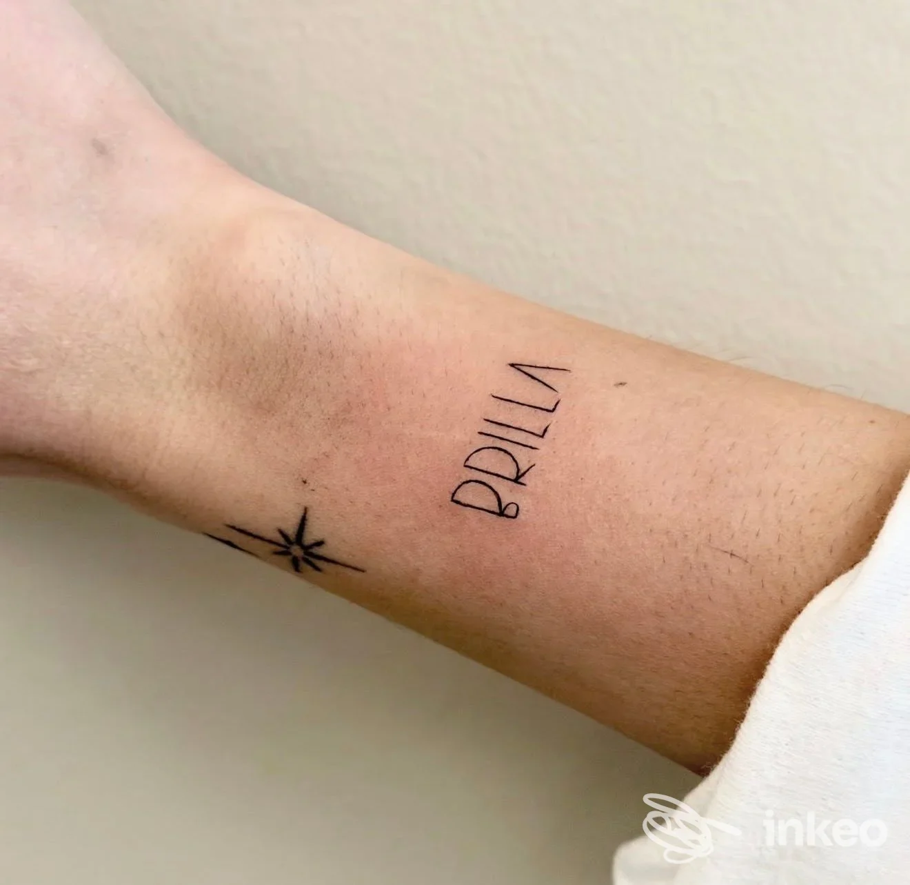 Tatuaggio sull'avambraccio: parola BRILLA in caratteri sottili accompagnata da una piccola stella stilizzata. Eseguito da Ventuno InkLab a San Lorenzo del Vallo, senza volto visibile né elementi di overlay sociale.