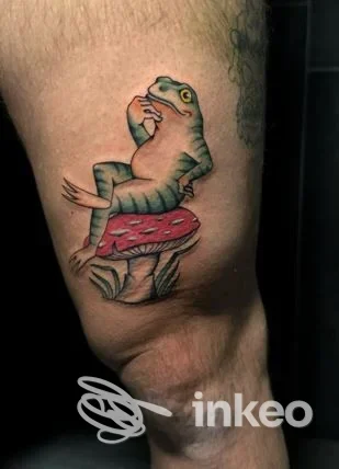 Tatuaggio colorato di una rana seduta su una grande fungo, realizzato su pelle visibile nella foto.