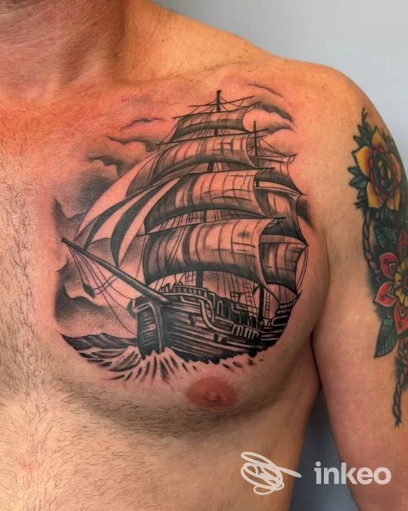 Tattoo realizzato sul torace sinistro: vela grande e dettagliata su pelle chiara, con altri tatuaggi visibili sul braccio, senza volto incluso nell’immagine.