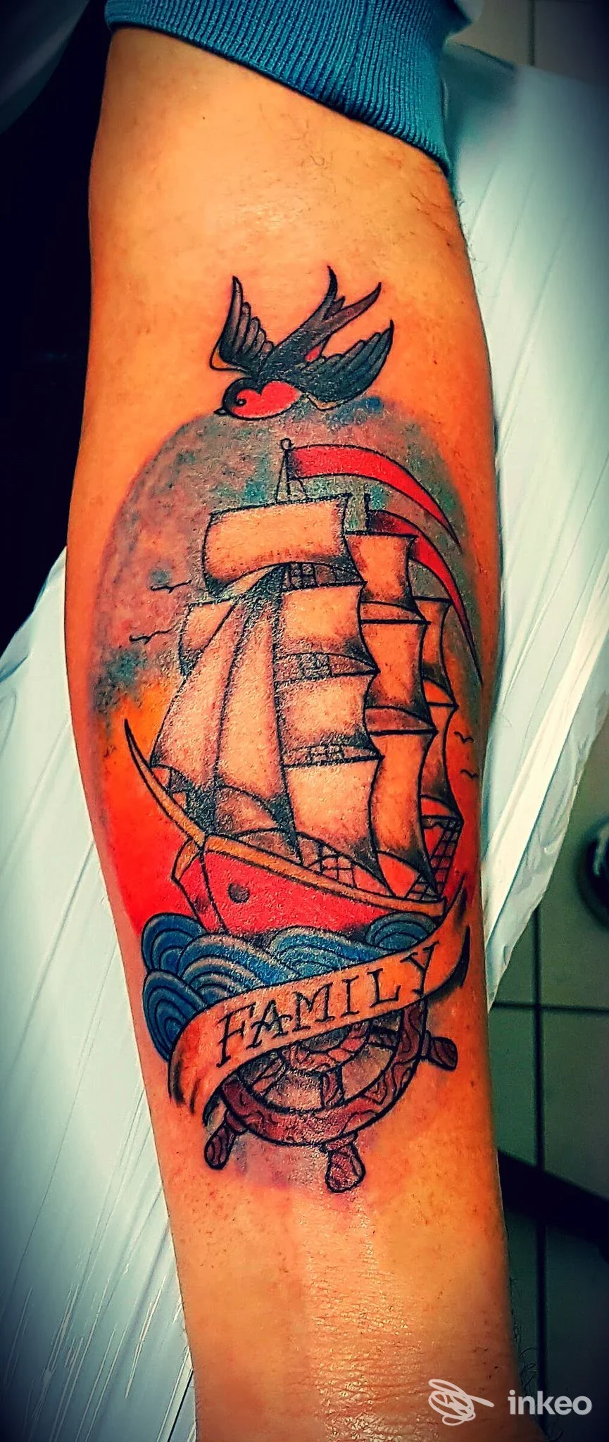 Tatuaggio realistico su avambraccio raffigurante una nave a vela con mare, ornamento con la scritta FAMILY; colori vividi e dettaglio netto, tatuaggio eseguito sulla pelle.