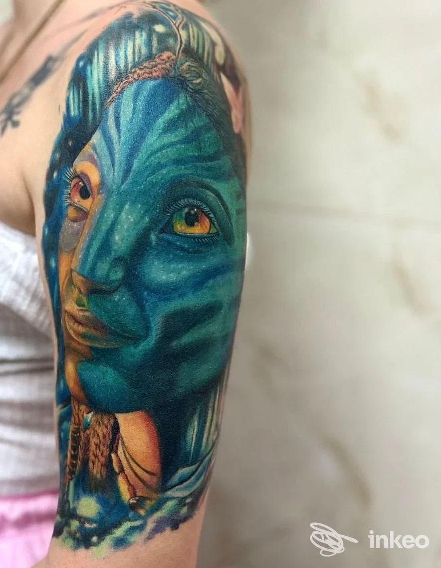 Tattoo a braccio con un volto blu intenso e dettagli colorati: arte corporea realizzata, mostrata su una persona presso uno studio Seven Ink a Quattromiglia.