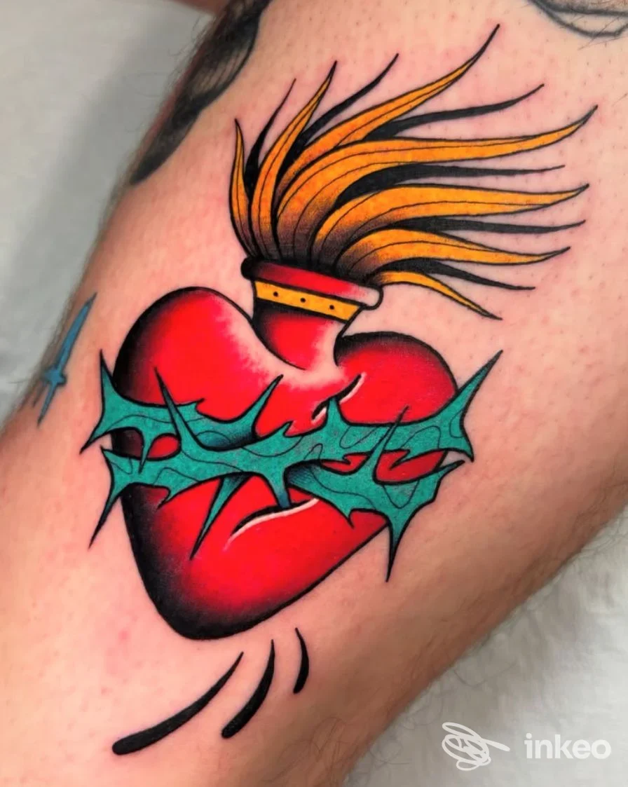 Tattoo su pelle di cuore rosso con contorno scuro e ornamenti verde-blu, con fiamma arancione in alto, visibile su braccio.