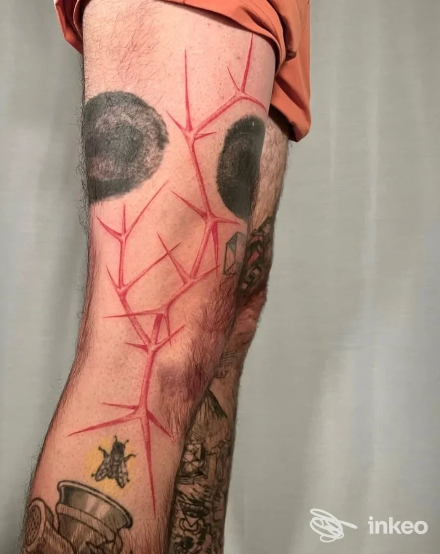 Tattoo visibile sulla gamba sinistra, rete ramificata di linee rosse su pelle, con aree scure al lavoro e un altro tattoo in basso. Studio Inkers Tattoo.
