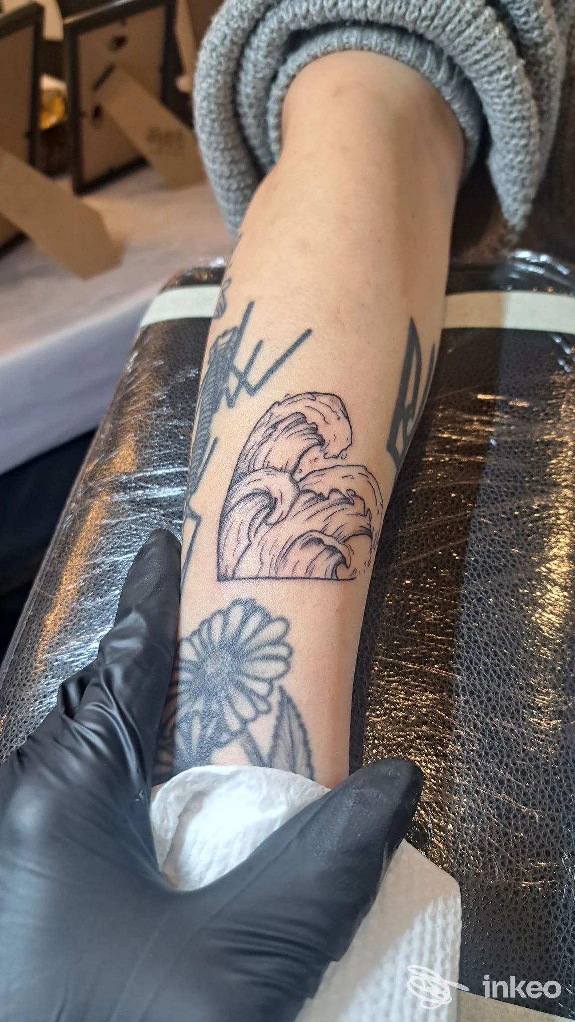 Braccio di una persona con tatuaggi floreali ben visibili, posizionato su tavolo da studio; sono presenti maniche di maglia e guanti neri. Ripresa a fuoco moderato a Reggio di Calabria al Fly Ink Studio.