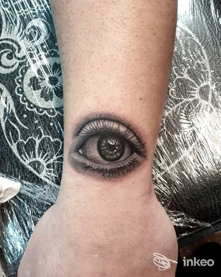 Tattoo realistico di un occhio inciso sulla pelle dell’avambraccio, visibile chiaramente senza volto umano interamente.