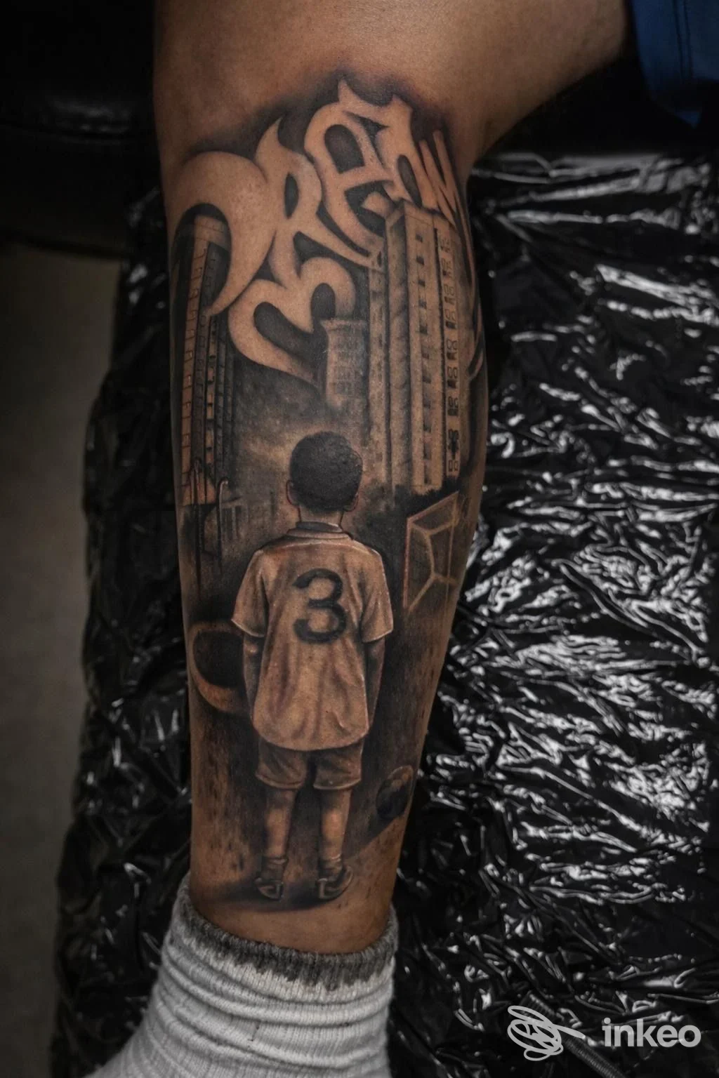 La Tinta Tattoo Studio, Sellia Marina: tatuaggio realistico su polpaccio raffigurante un ragazzo visto di spalle, di fronte a edifici, con la maglietta numerata 3.
