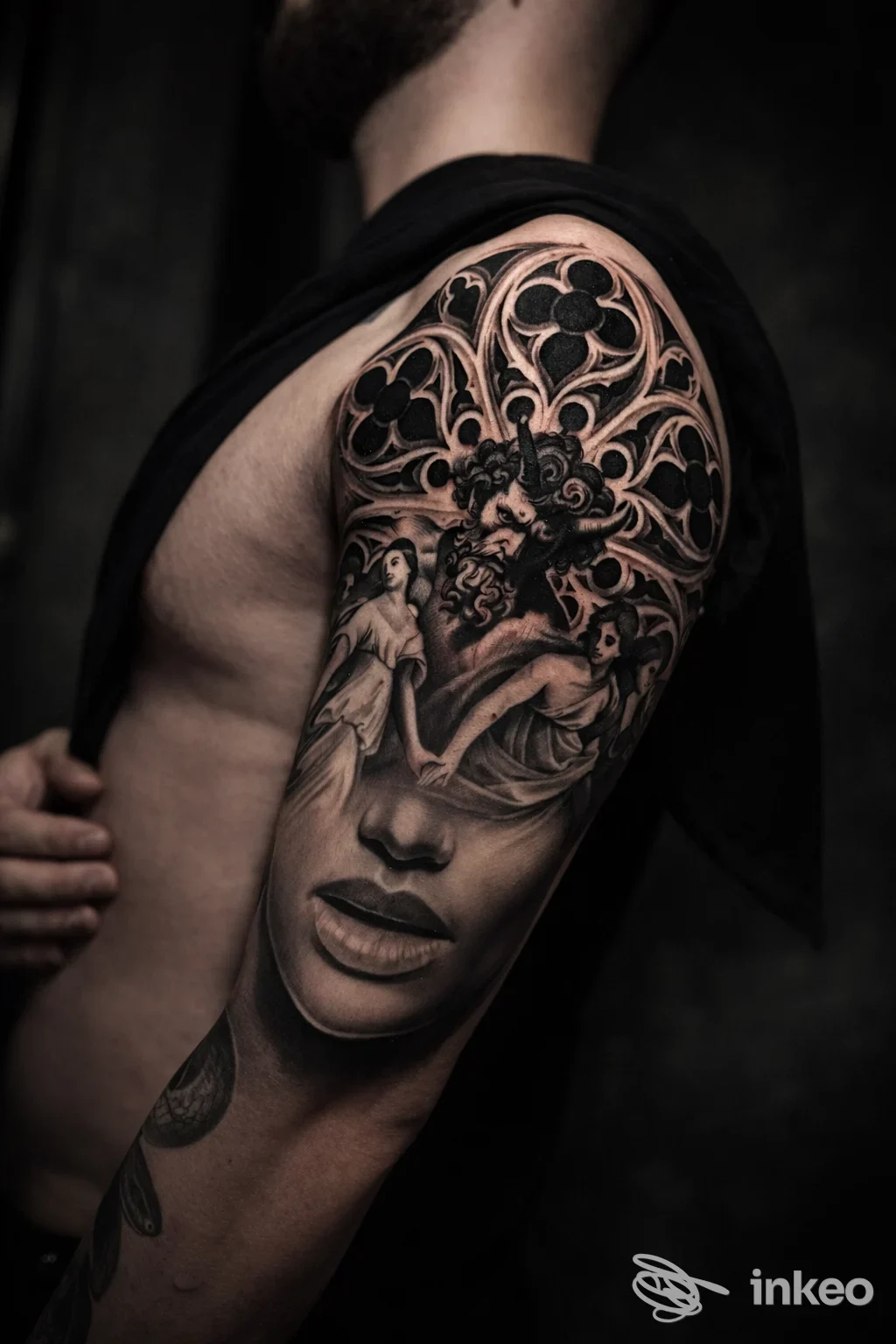 Braccio maschile con tatuaggio realistico in bianco e nero, mostra un volto femminile e motivi floreali complessi lungo la spalla e l’avambraccio.