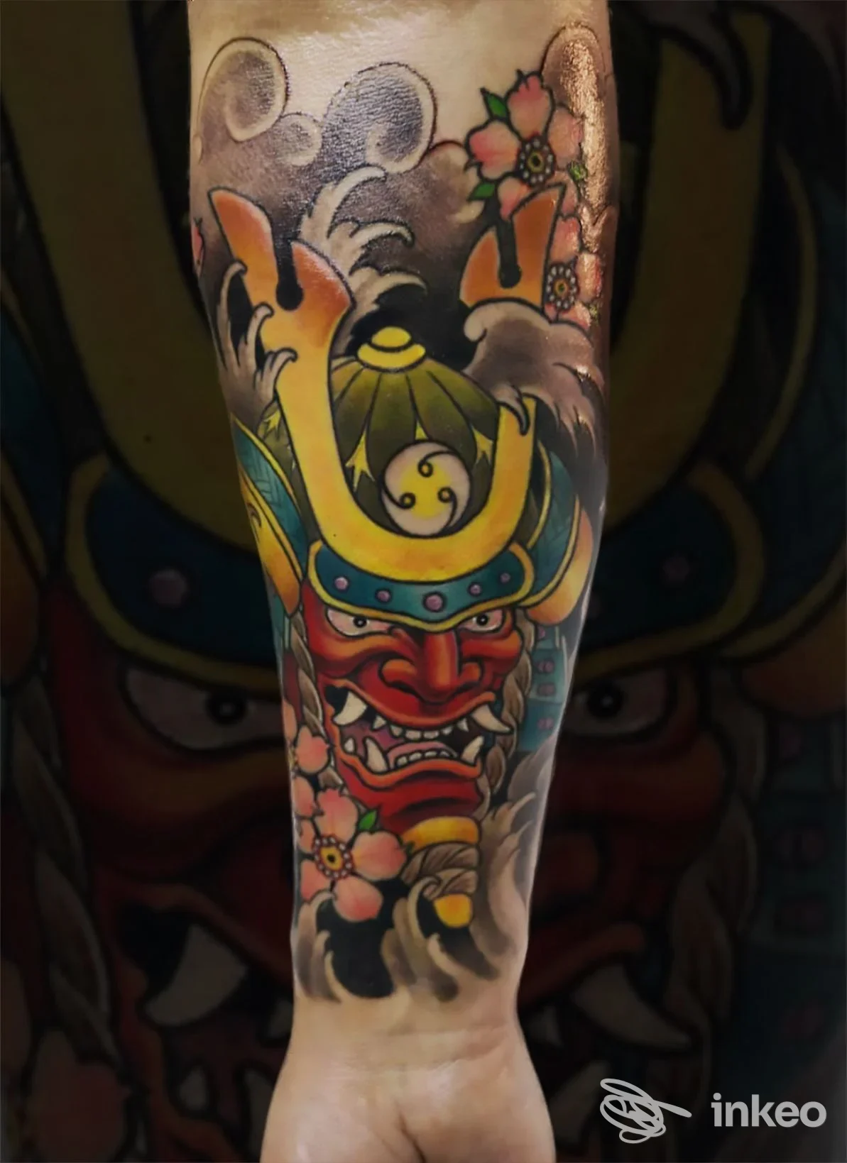 Tattoo a tutta gamba raffigurante un demone giapponese (oni) con casco e colori vivaci, accompagnato da fiori sul lato, realizzato sulla pelle.