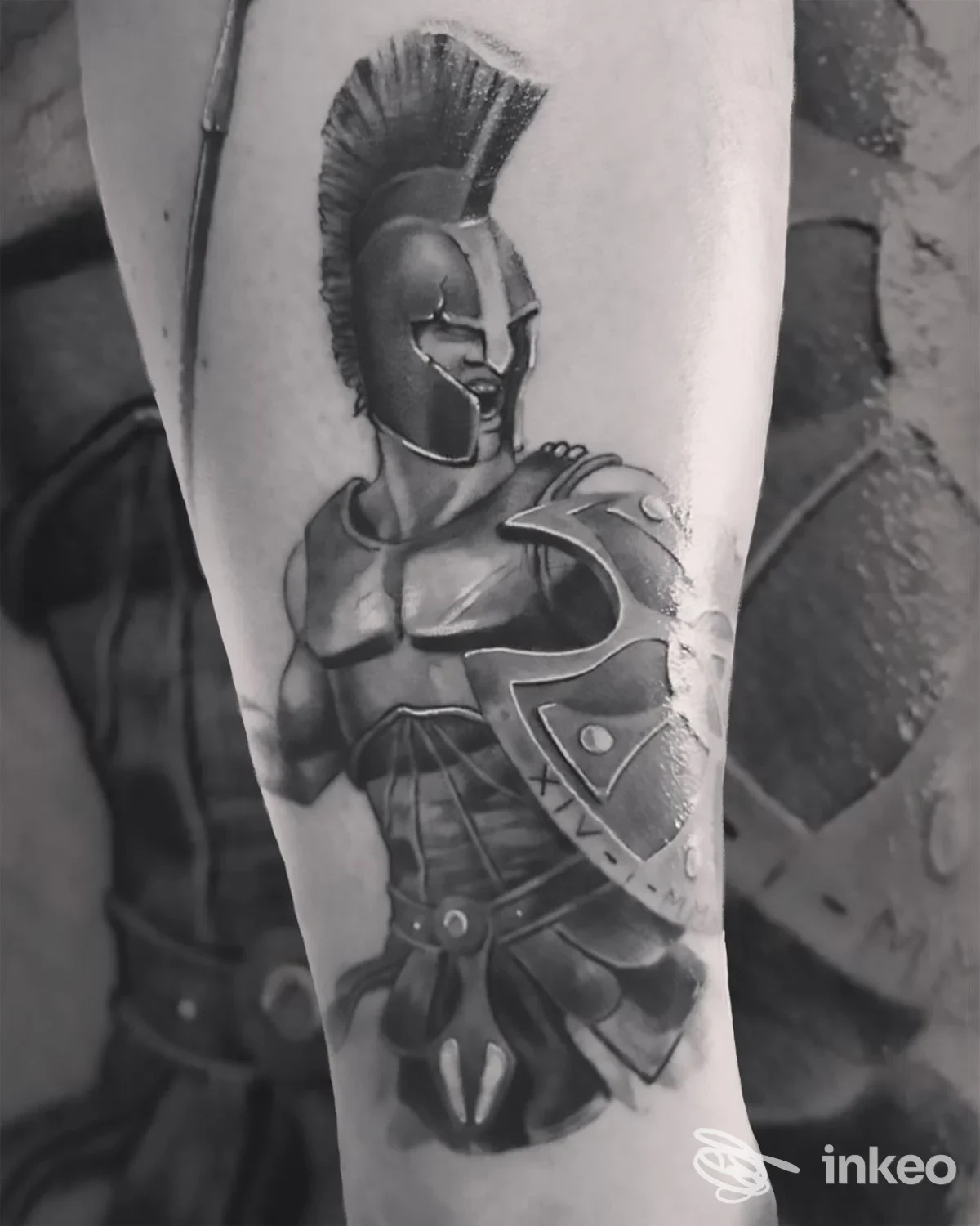 Tattoo di un guerriero in armatura con elmo con cresta sul braccio, tonalità grigie, dettagliando corazza e scudo in stile realistico.