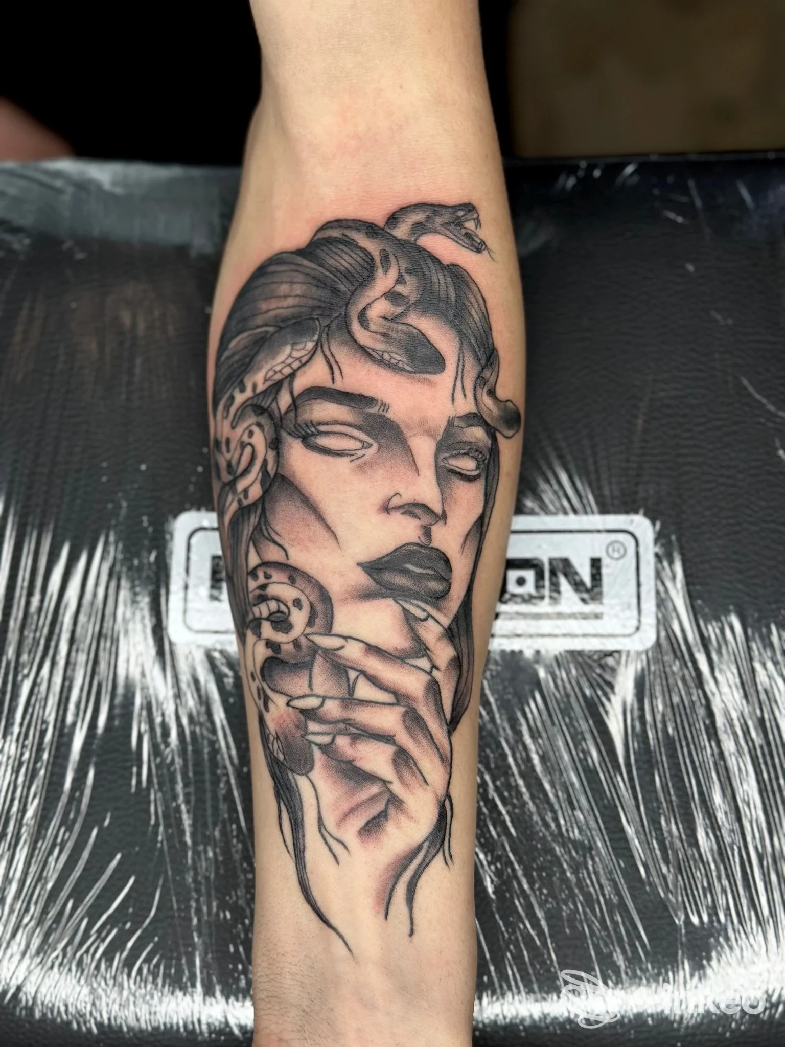Tattoo realistico su avambraccio raffigurante un volto femminile con mani e dettagli inchiostrati, stile grafico in bianco e nero, visibile su pelle reale.