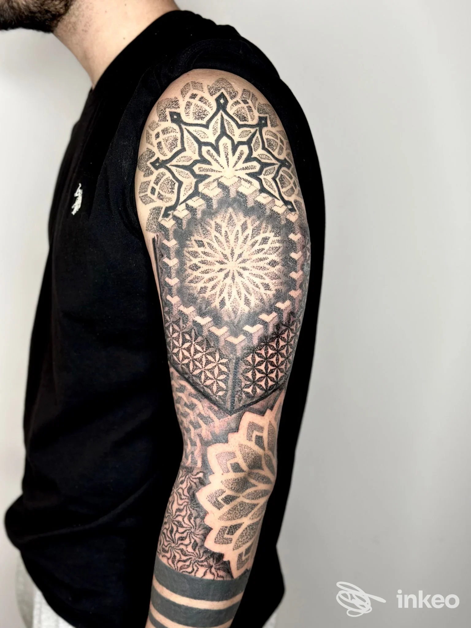 Tatuaggio geometrico a mandala in bianco e nero sul braccio di un uomo, con linee nette e sfumature grigie, visibile da spalla al polso.