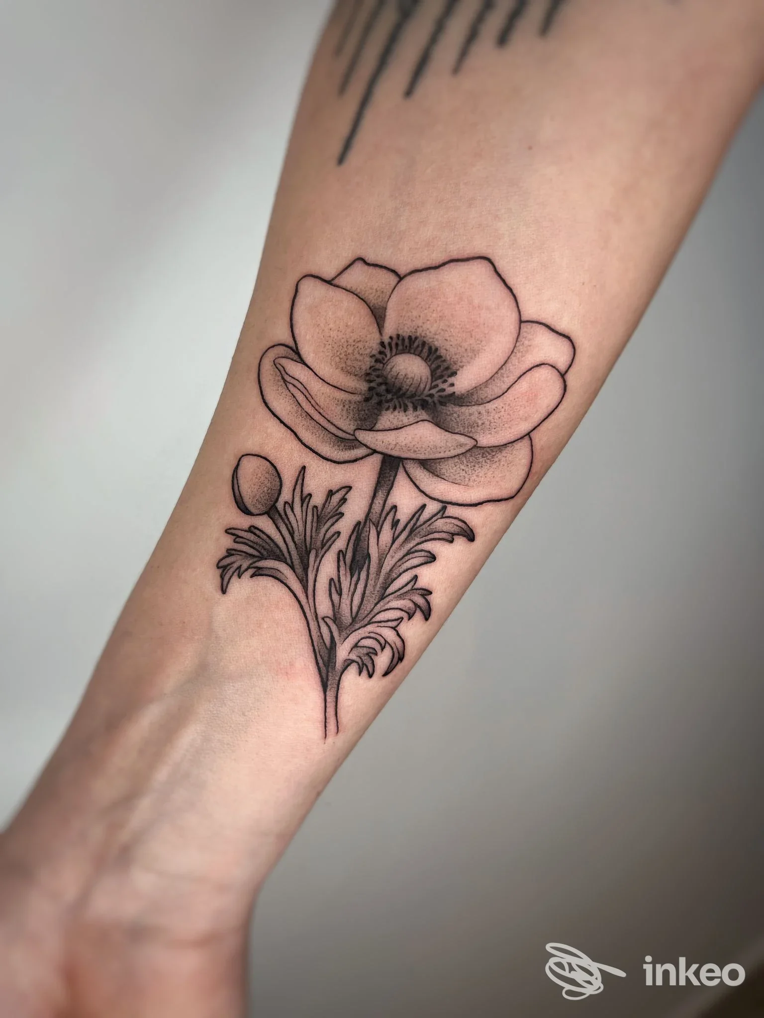Tattoo visibile sull’avambraccio: fiore stilizzato in linework su pelle chiara; realizzato presso Orion Tattoo Studio, Montalto Uffugo.