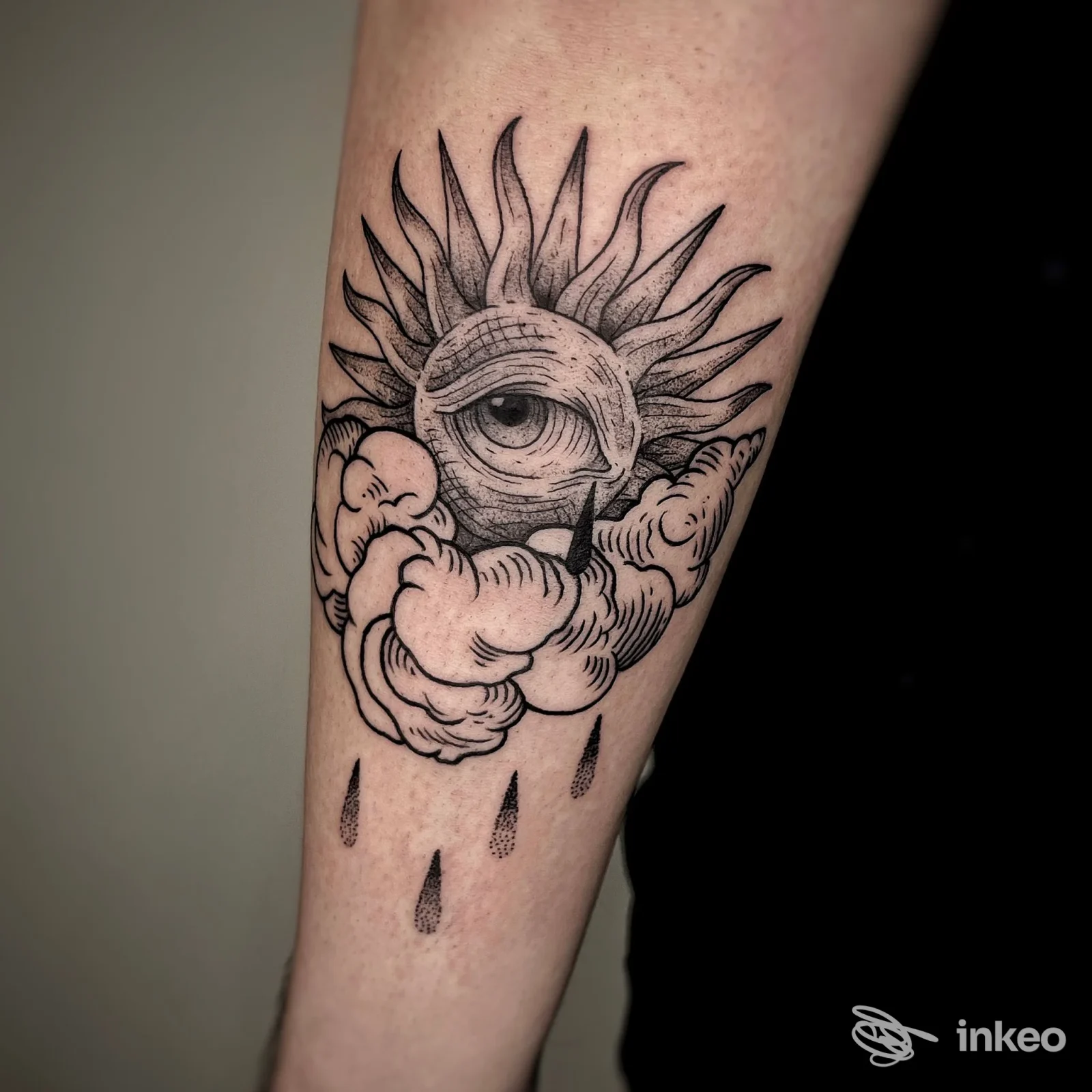 Tattoo sul braccio raffigurante un sole con un occhio al centro tra nuvole e gocce di pioggia, realizzato da Orion Tattoo Studio a Montalto Uffugo.