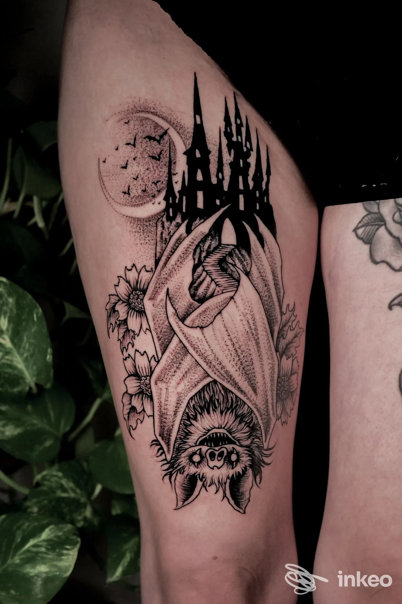 Tattoo su gamba raffigurante un pipistrello con castello in rilievo sopra, luna e fiori intorno, realizzato sulla pelle.