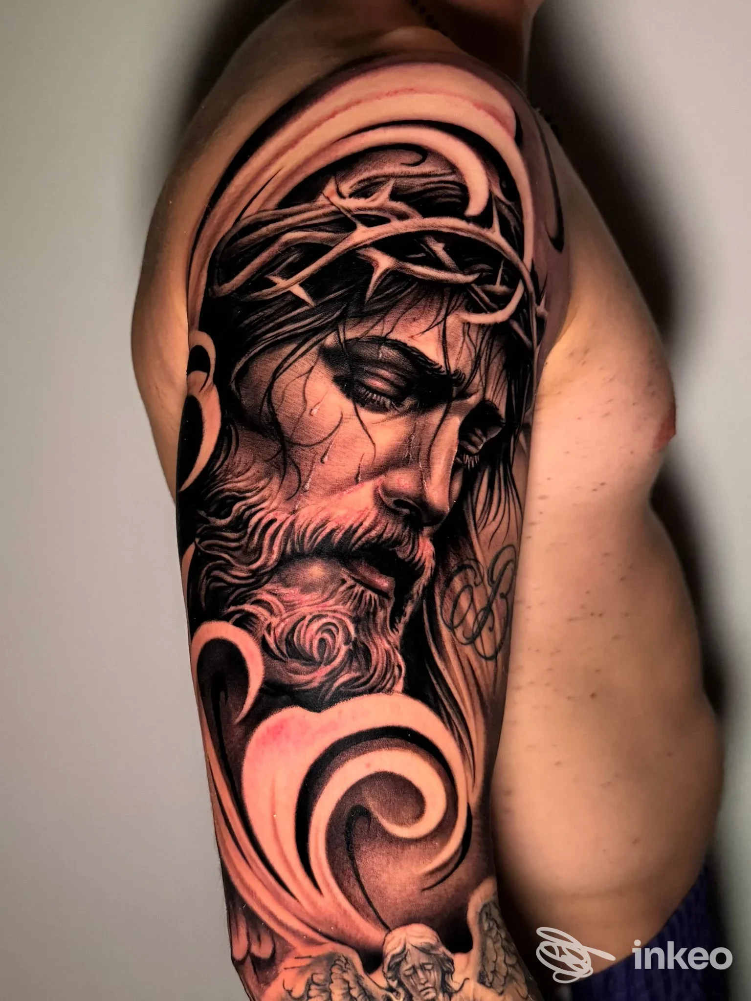 Tattoo realistico su braccio raffigurante Gesù con corona di spine, tonalità scure e rosa, visibile su pelle nuda.