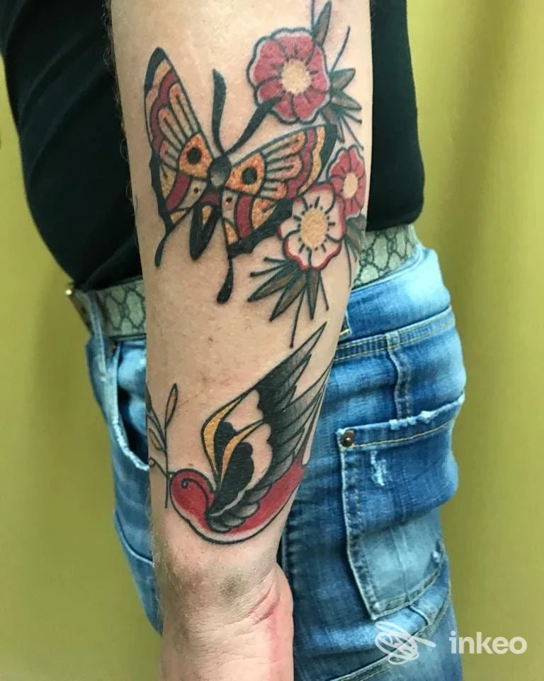 Tattoo visibile sull'avambraccio: una farfalla stilizzata e fiori, realizzato presso Raffaele Ink Guerrasio a Gioia Tauro, senza persone visibili.