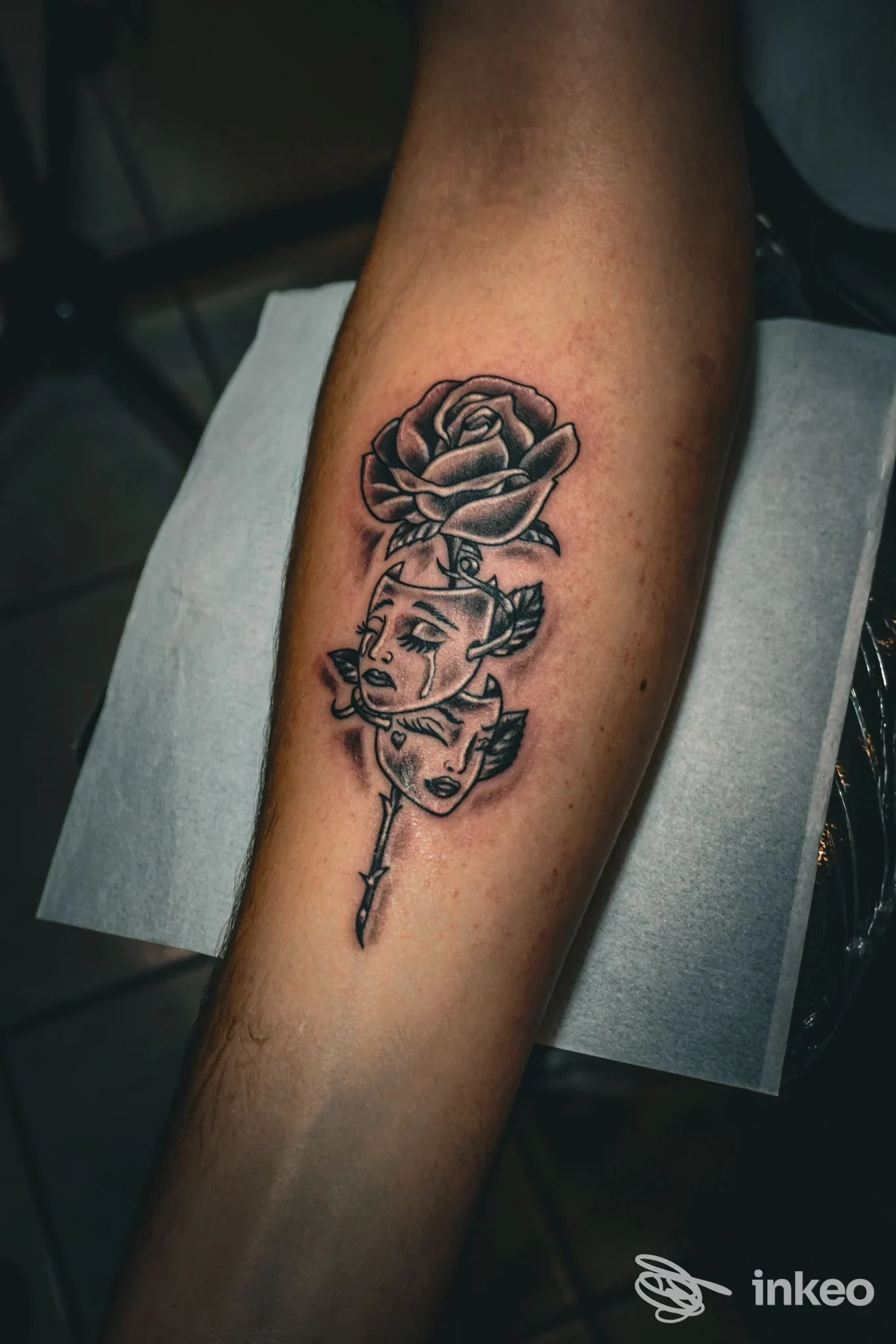 Avambraccio con tatuaggio: una rosa in alto e volti stilizzati intrecciati con un pugnale sottostante, linee nette e ombre manga. studio InkFinity Tattoo, Amantea.