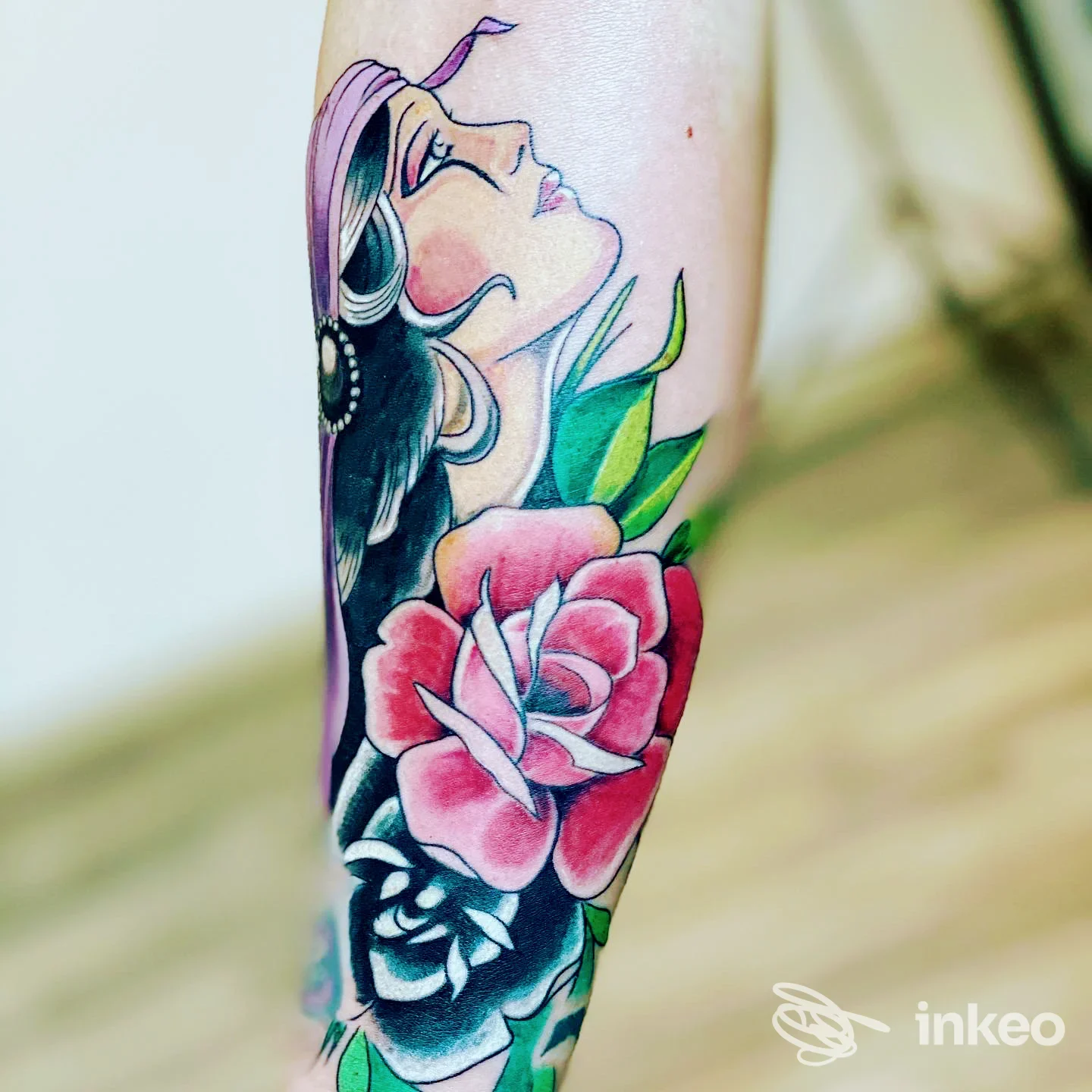 Mezzo braccio con tatuaggio a tema donna e fiori colorati, visibile su pelle chiara, in primo piano con sfondo sfumato.