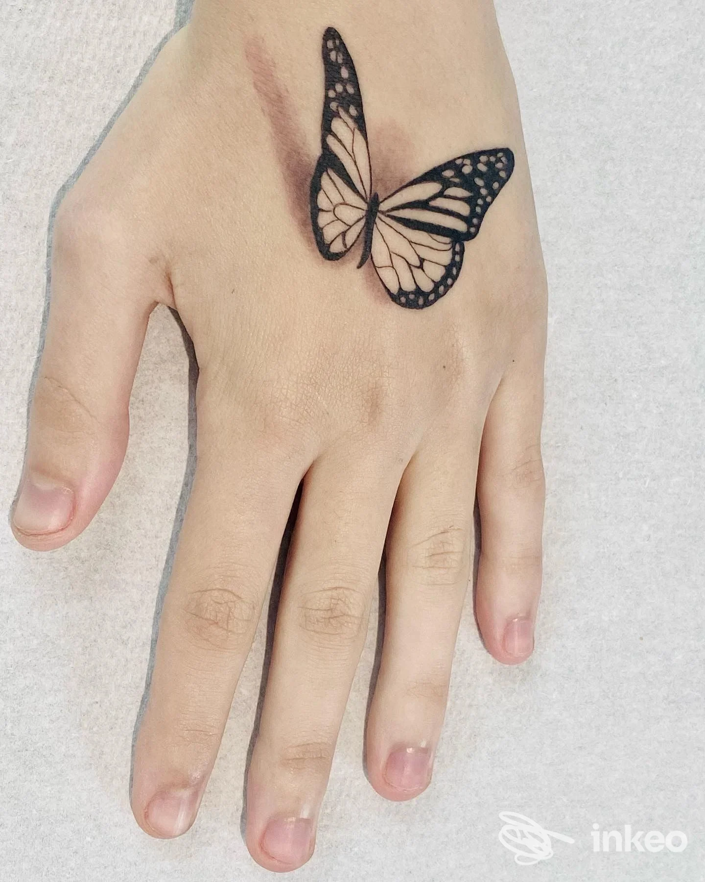 Tattoo su una mano, farfalla nera e bianca ben delineata sulla pelle.