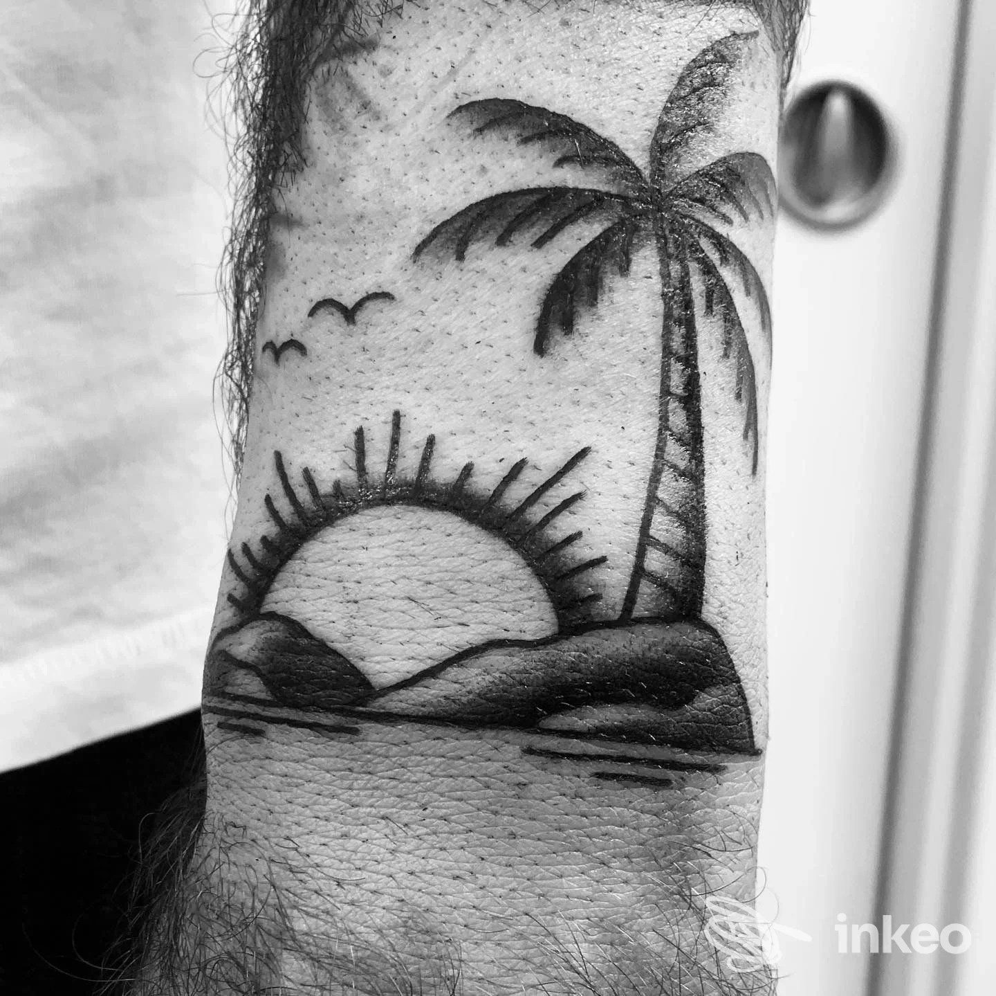 Tatuaggio su avambraccio raffigurante tramonto al mare con palma, realizzato presso Clinic Tattoo & Piercing, Roccella Ionica.