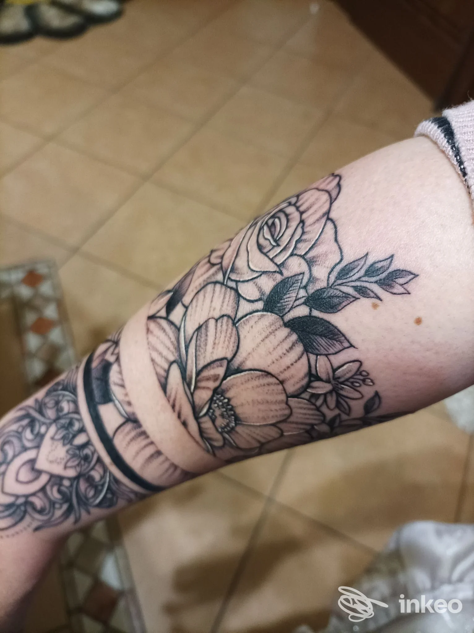 Tattoo floreale in bianco e nero sull'avambraccio, realizzato direttamente sulla pelle, visibile su sfondo pavimentato; studio Gigiz Tattoo Art Studio, San Nicola Arcella.
