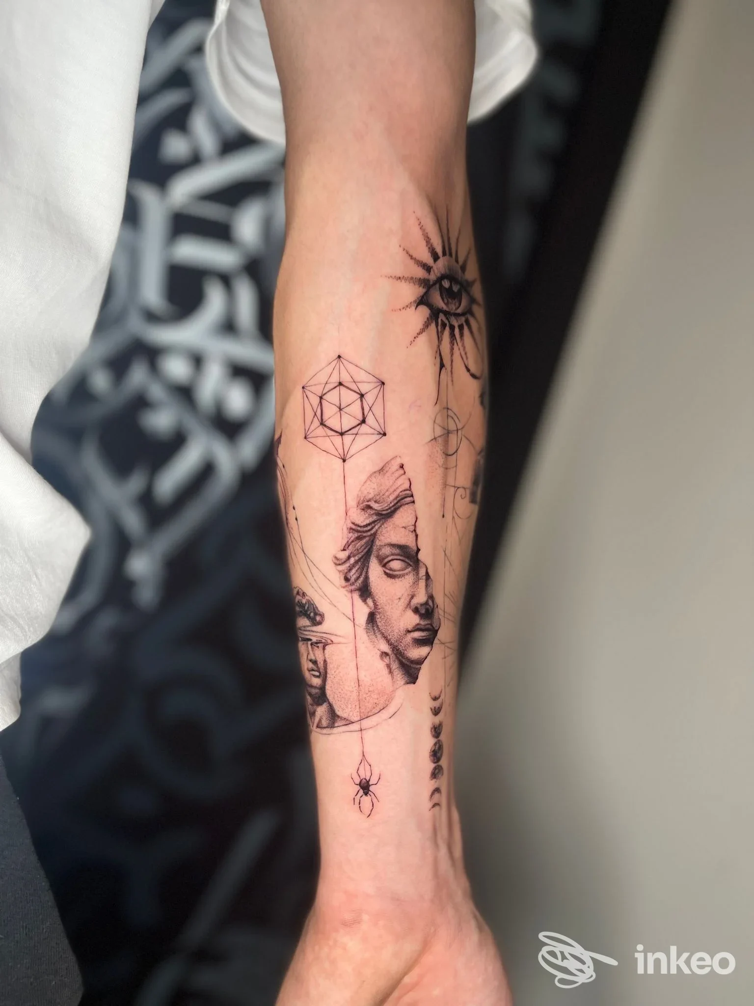 Braccio umano con vari tatuaggi geometrici e figure, tra cui volto, sole stilizzato e motivi geometrici; colori neri su pelle chiara.