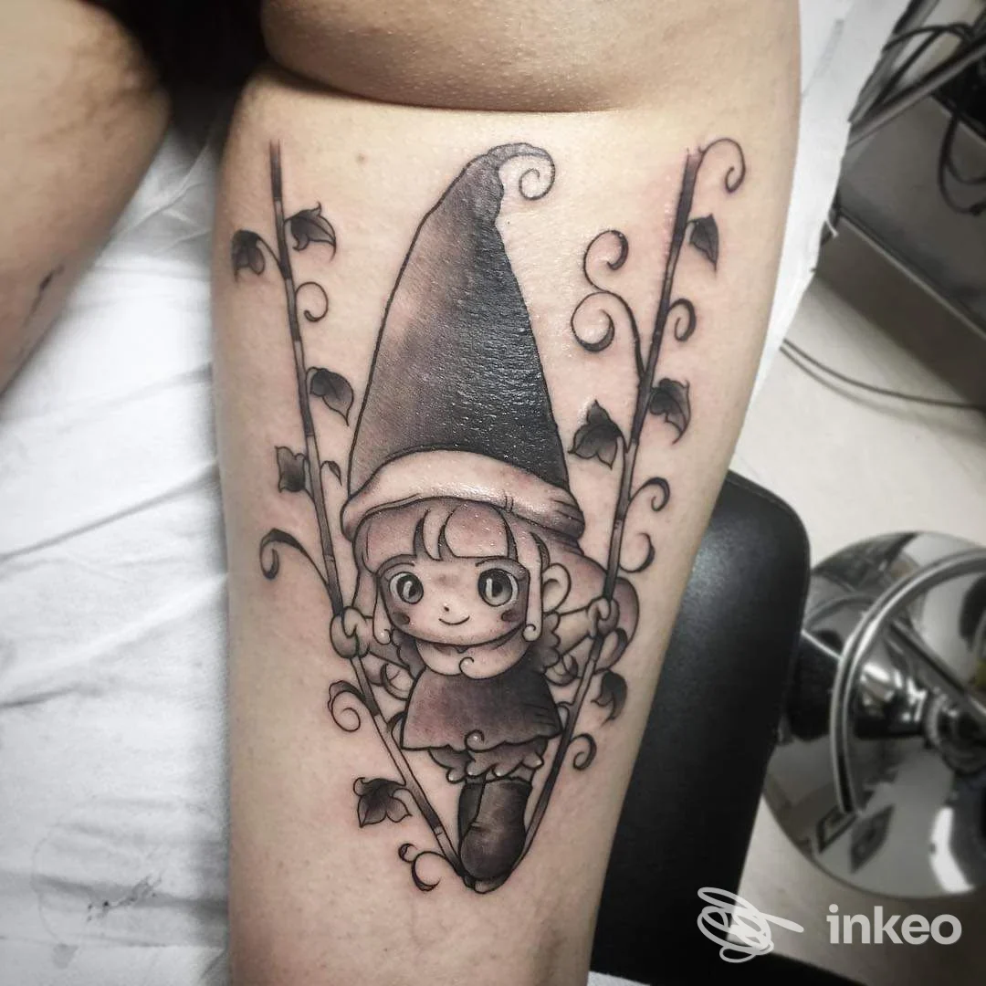 Tattoo su polpaccio raffigurante un gnomo in cappello, seduto su una altalena circondata da rami e foglie, eseguito da Oreste Coscia a Castrovillari.