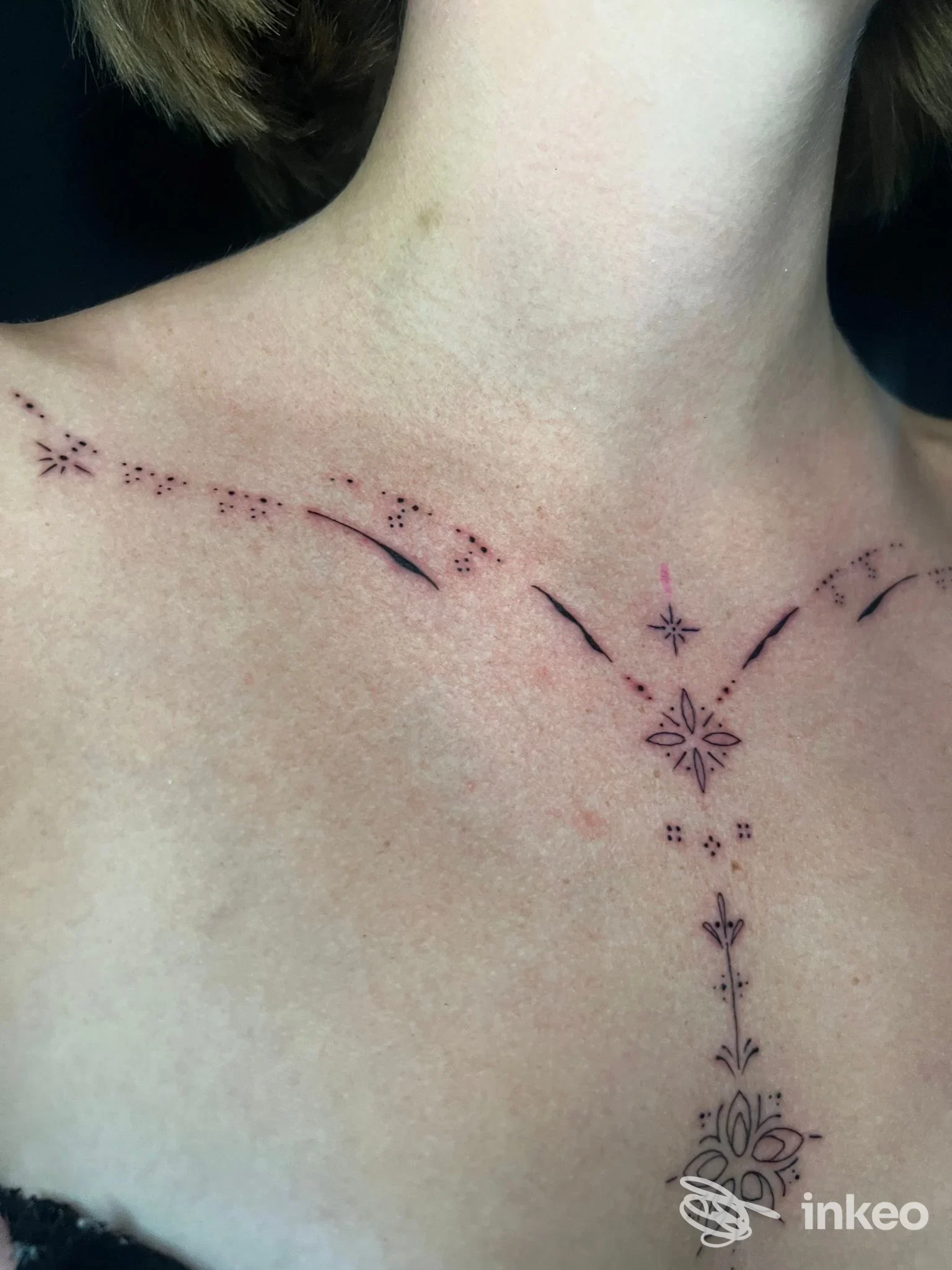 Collo con tatuaggio decorativo lungo la linea centrale del décolleté: linee puntiformi e motivi floreali stilizzati, eseguiti sulla pelle. nulla che suggerisca interfacce o contenuti non tattili; firma dello studio Black Dalia Tattoos, Reggio Calabria.