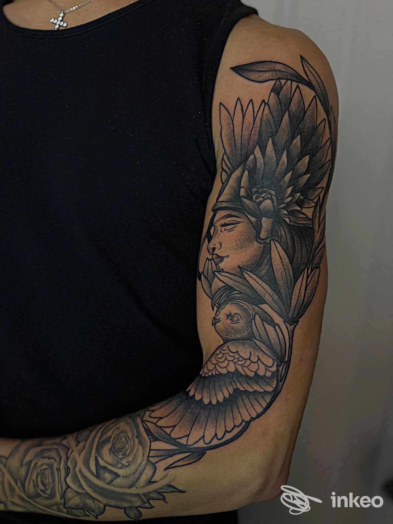 Tatuaggio sull'avambraccio in bianco e nero raffigurante volti e ornamenti con uccello e fiori, eseguito direttamente sulla pelle.