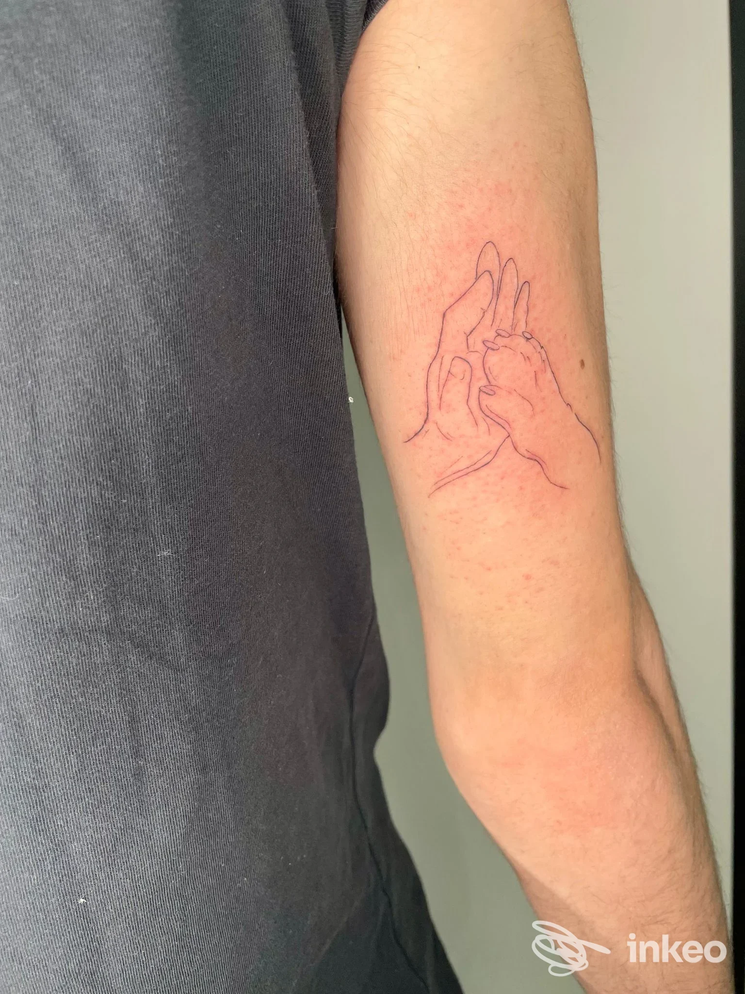 Anteprima di un braccio: tatuaggio a linee rosse che raffigura due mani che si stringono, disegno contornato sulla pelle.