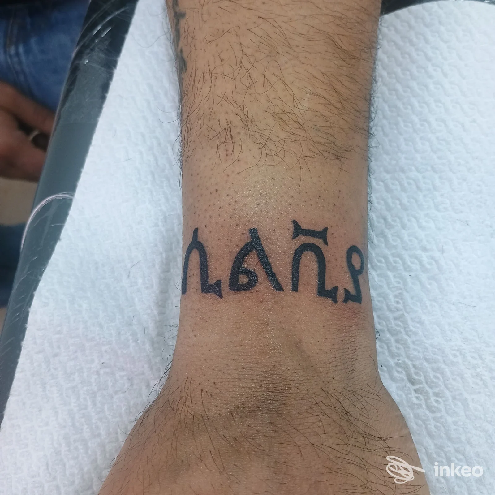 Avant-braccio sinistro con tatuaggio nero in stile caratteri gotici, visibile su pelle chiara, senza persona presente nell’immagine.